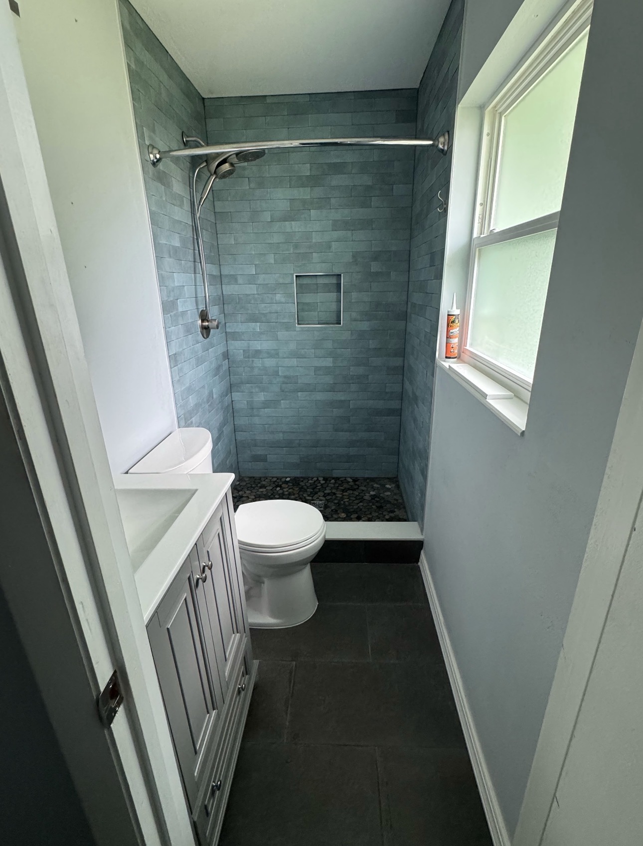 After: blue shower wall tiles, a recessed niche, pebble shower floor, and dark floor tiles
