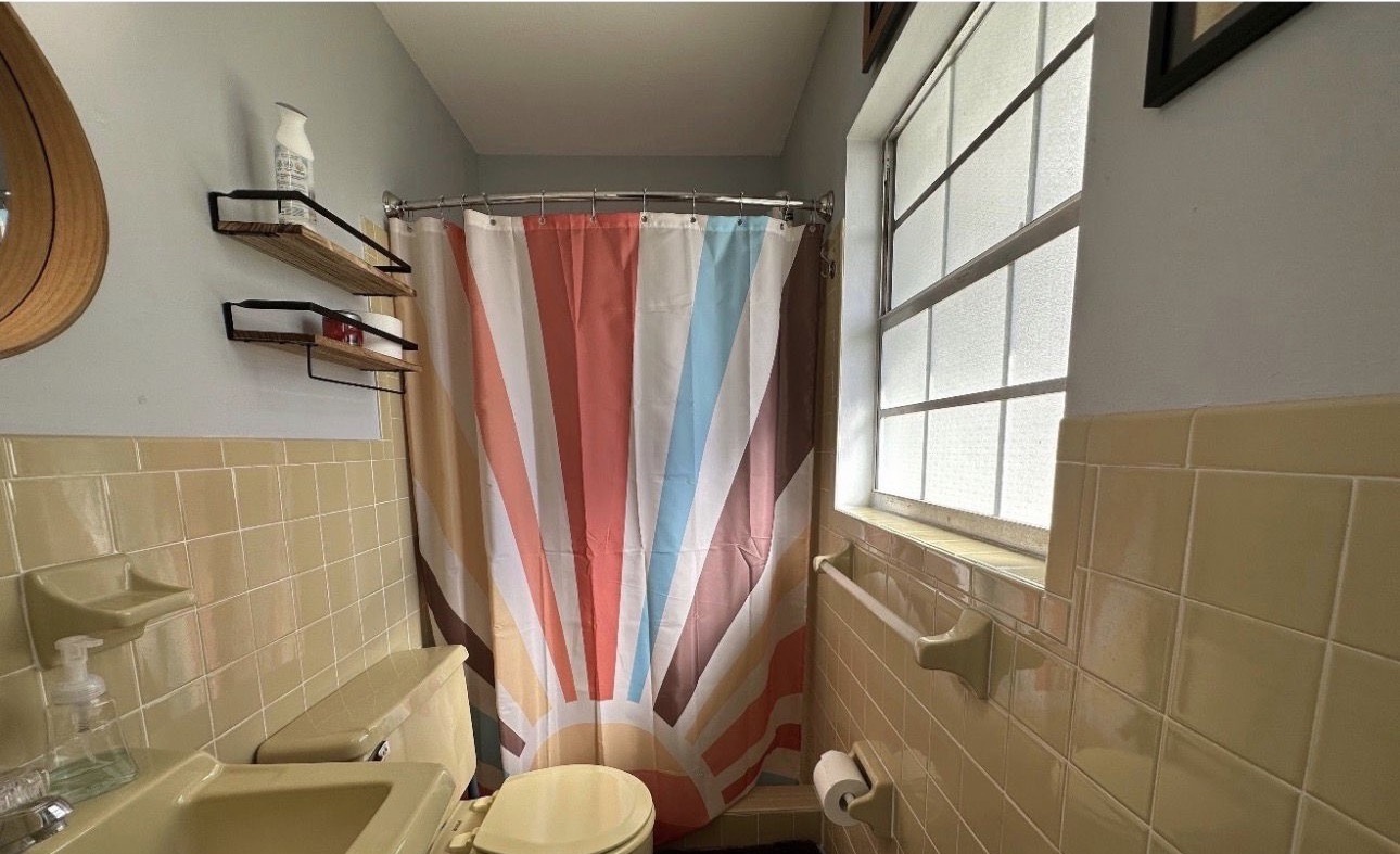 Before: bathroom with yellow wall tiles and a striped shower curtain